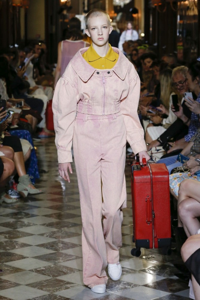 девушка с очень короткой стрижкой и чемоданом демонстрирует модный дорожный костюм весна 2019 с брюками и жакетом оригинального фасона