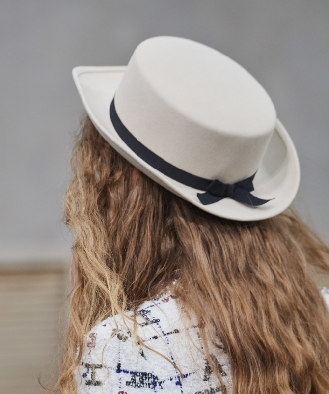 белая женская шляпа с плоской тульей в виде таблетки, черной лентой и небольшими полями чуть загнутыми вверх - фото с модных показов Шанель весна-лето 2020 года