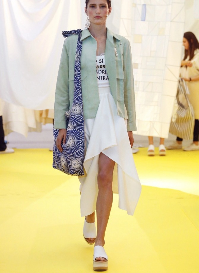 уличная весенняя мода 2020 для девушек - куртка-жакет пастельных тонов, белая юбка с неровным подолом, футболка с плакатным принтом. белые босоножки на очень высокой платформе , сумка-мешок через плечо с контрастным по цвету рисунком - образ с модного показа Madrid Spring 2020