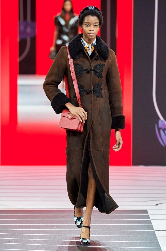 Зимняя одежда из овчины. Модная дубленка 2021 года от Prada - темно-коричневая с черным воротником и черными передними аппликациями-застежками, с манжетами из черного меха на рукавах. 