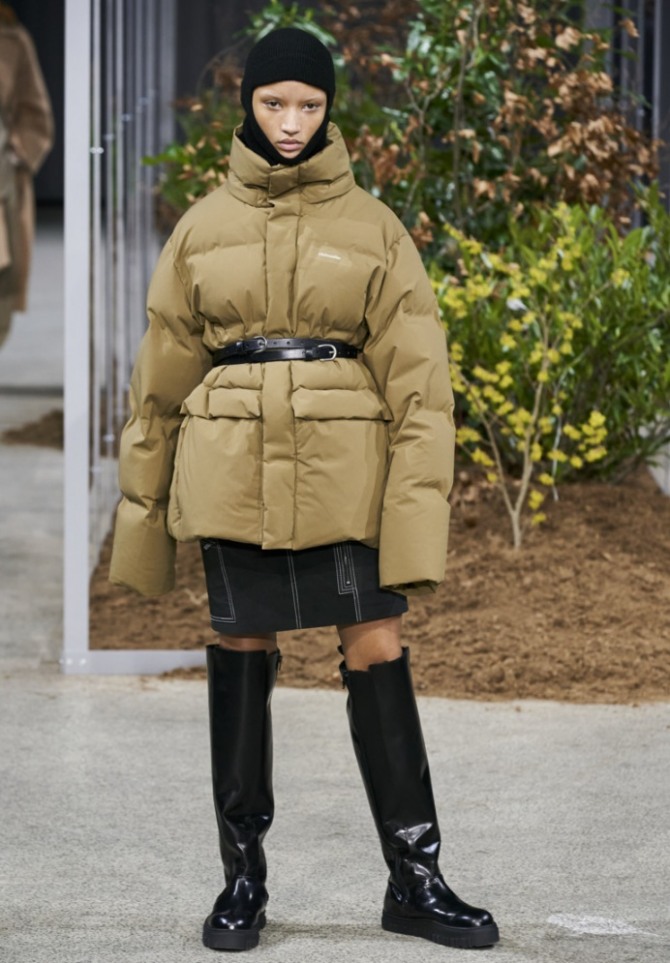 фото модных пуховиков сезона зима 2021 года с подиума - короткая модель бежевого цвета от бренда Holzweiler - с кожаным черным пояском на талии и удлиненными рукавами