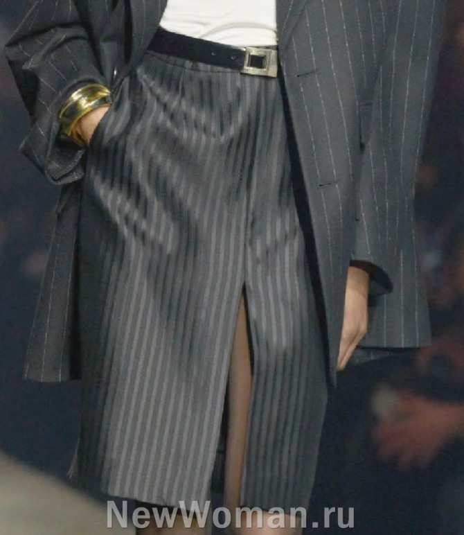 главные тенеднции в моде на женские юбки 2024 года - деловая повседневная модель юбки из мужской костюмной ткани в серо-черную полоску, длина чуть выше колена, высокий разрез посередине полотна юбки, ремень с пряжкой на талии