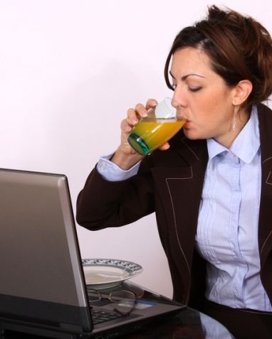 женщина ест и пьет сок, сидя за компьютером