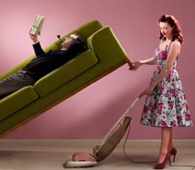 женщина с пылесосом, а мужчина на диване читает