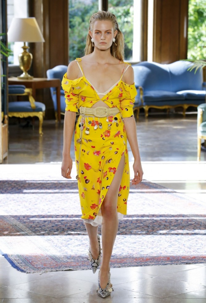 летний образ лето 2019: желтое платье с открытой грудью, с высоким разрезом на юбке и плетеным ремнем, клипсы белого цвета, а туфли со змеиным принтом