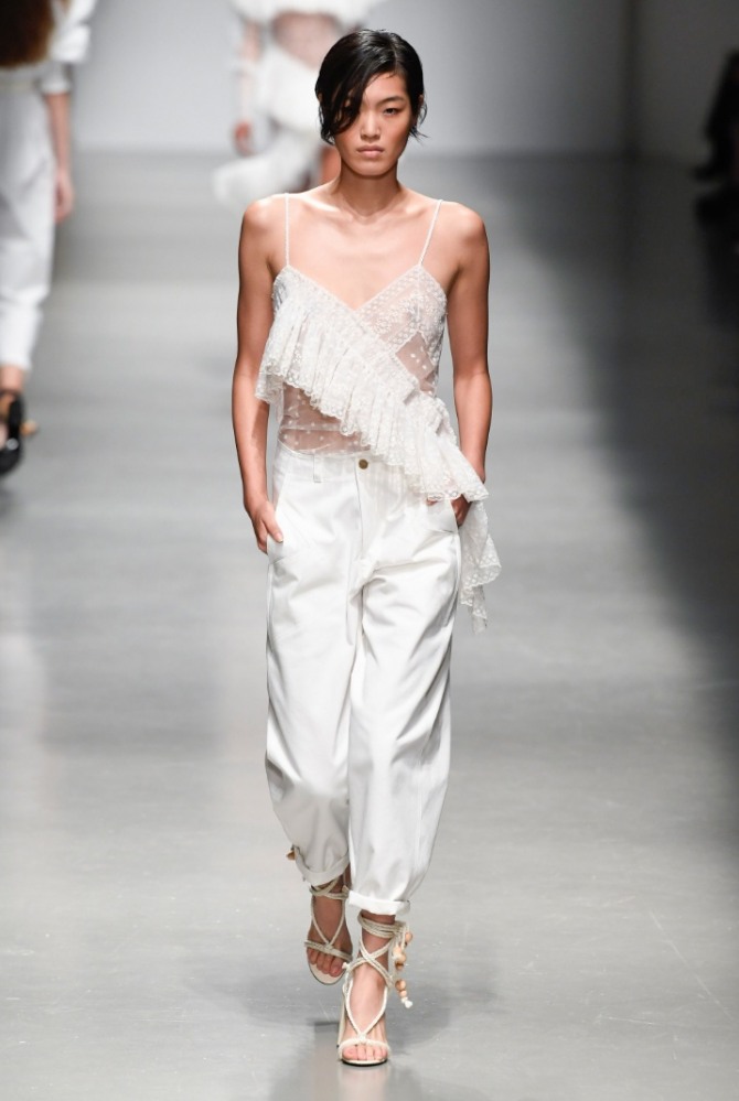 супер модный летний женский образ 2019 года: широкие, зауженные книзу белые брюки с подворотами, босоножки с лентами выше щиколоток, топ из тюля с воланом
