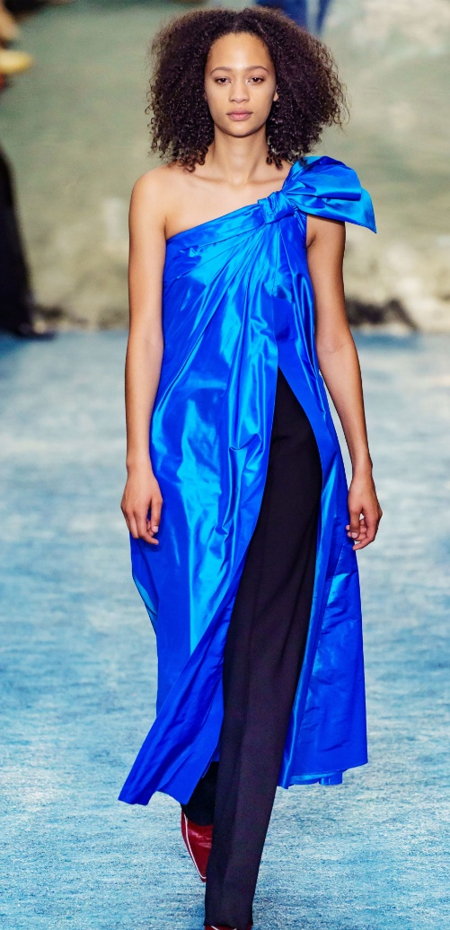 ярко-синее вечернее платье с асимметрией на одно плечо, надетое поверх черных брюк, декорированное половинчатым бантом на плече