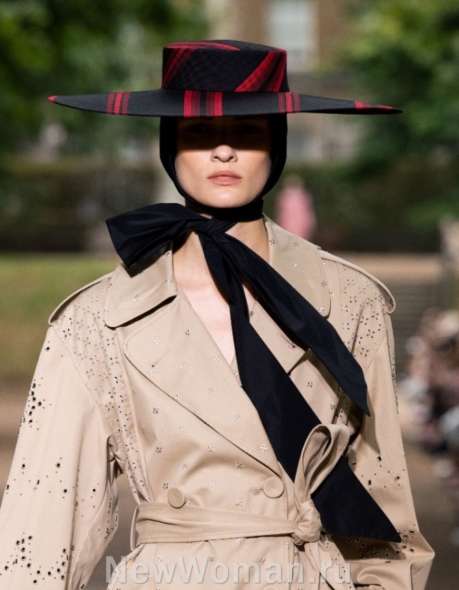 стильный образ на весну 2020 года - черная шляпа в красную полоску с плоскими полями, надетая на черный платок исветло-бежевый плащ с перфорацией, люверсами и стразами от бренда Erdem