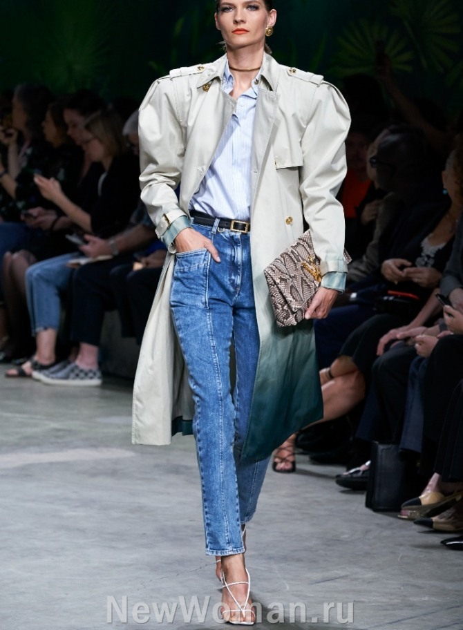 темно-голубые женские брюки скинни из джинсовой ткани длиною 7/8 с передними накладными карманами и коричневым узким кожаным ремнем в комплекте с серым плащом миди - фото с модных показов весна-лето 2020 года от Versace